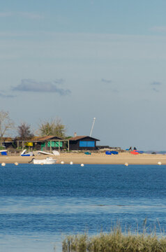 View of a tranquil coastline with wooden shacks nestled on the sandy beach, where boats rest and the serene blue water meets the shore, Arcachon, France.