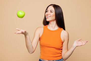 Young smiling happy woman wear orange casual clothes hold in hand eat toss up green apple isolated on plain pastel light beige background. Proper nutrition healthy fast food unhealthy choice concept.