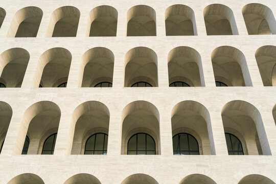 View of repeating arches cast shadows, creating a mesmerizing pattern on the facade, hinting at the grand scale of the building, Rome, Lazio, Italy.
