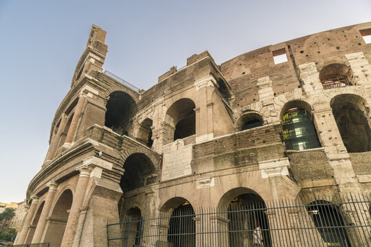 View of the ancient Colosseum's weathered facade rises against the pale sky, its arches and stone telling tales of gladiators, Rome, Lazio, Italy.