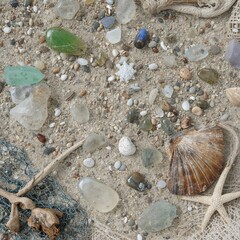 Assorted sea glass pieces colorful pebbles a shell starfish and netting scattered on sand