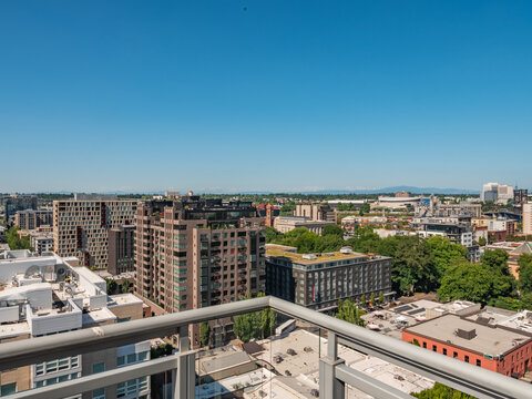 View of the city unfolds under a clear blue sky, framed by the silver railing, with modern buildings and lush trees blending in the distance, Portland, Oregon, United States.