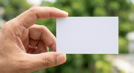 Close-up of hand holding blank white business card mockup against blurred green nature background