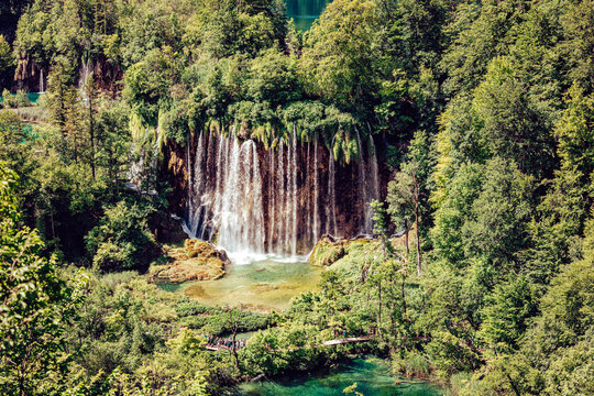 View of cascading waterfalls plunge into a crystal-clear turquoise pool, embraced by vibrant green foliage, a serene escape into nature's embrace, Plitvicka Jezera, Lika-Senj County, Croatia.
