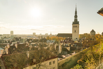 View of the sun shining over red tiled roofs and spired church towers creating a warm glow across the cityscape, Tallinn, Harju County, Estonia.