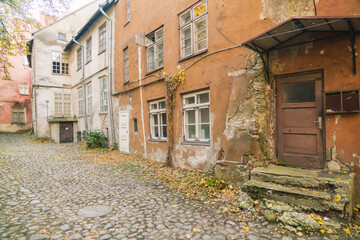 View of weathered buildings with peeling orange paint and stone steps meet a textured cobblestone ground scattered with fallen leaves, Tallinn, Harju County, Estonia.
