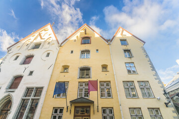 View of historic buildings with pointed roofs stand tall against a blue sky, flags hanging below windows in Tallinn, Harju County, Estonia.