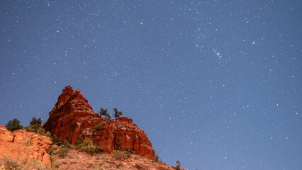 View of red rock formations jutting boldly against a dark sky filled with countless stars, creating a stunning contrast of earthly tones and celestial light, Sedona, Arizona, United States.