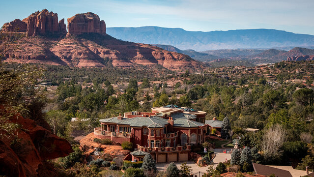 View of a grand estate nestled amidst the red rock formations and lush greenery, under a vast blue sky, creating a striking contrast in Sedona, Arizona, United States.