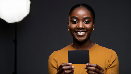 Smiling woman holding a blank black card in a professional studio setting with dark background, ideal for premium branding, luxury marketing, minimalist advertising, and modern promotional concepts
