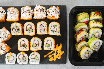 Assortment of sushi rolls including fried and avocado-topped versions, arranged on a black slate.
