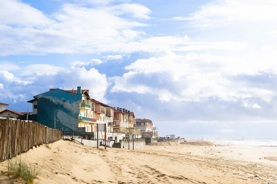 View of beachside houses with colorful facades meet the golden sand under a vast, cloud-strewn sky, offering a peaceful coastal scene, Hossegor, Nouvelle-Aquitaine, France.