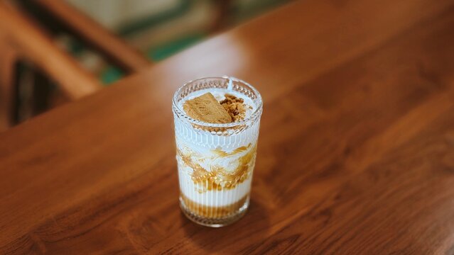 Aesthetic Iced Biscoff Coffee Latte with Creamy Milk, Creamy layered lotus biscoff latte in a glass with a biscuit, sweet indulgence on a wooden background, 