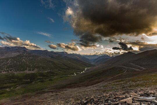 View of majestic mountains cloaked in shadows and light, with a winding river snaking through the verdant valley under a dramatic sky, Naran, Khyber Pakhtunkhwa, Pakistan.