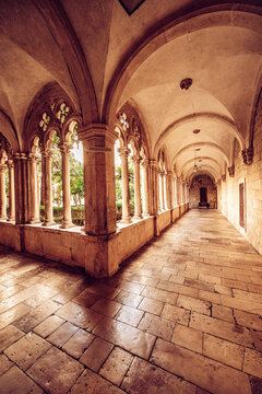 View of the aged stone corridor, with its arched ceilings and ornate windows, casts long shadows on the textured floor, Dubrovnik, Dubrovnik-Neretva County, Croatia.