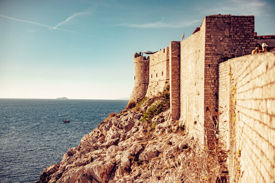 View of ancient stone walls meet the endless blue sea under a pale sky, a fortress perched on rocky cliffs guarding the horizon, Dubrovnik, Dubrovnik-Neretva County, Croatia.