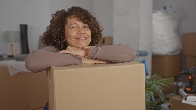 Woman leans with folded arms on packing box inside new building, gazing upward with calm expression in empty room; anticipation.