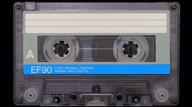 Audio Cassette Reels Spinning. Retro compact cassette tape with spinning reels on black background.	
