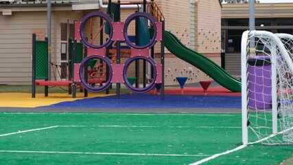 A colorful playground area on an Australian primary school campus featuring climbing frames, slides, and soft-fall safety surfacing beside a small soccer goal. Outdoor play, physical development. - Powered by Adobe
