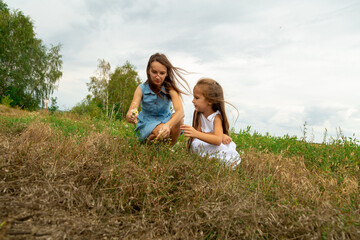 Fototapeta premium Mother and daughter picking daisies in a field on a summer day