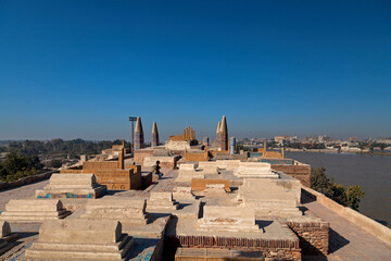 View of ancient tombs standing silently against the clear blue sky, a testament to time, overlooking the tranquil river, , Sukkur, Sindh, Pakistan.