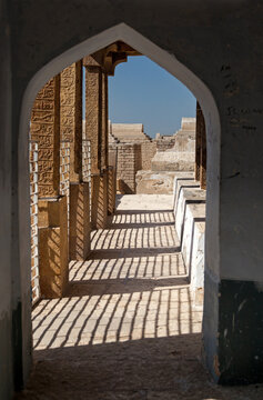View of rhythmic shadows cast by pillars through an arched doorway, revealing sun-baked walls and ancient architecture, Sukkur, Sindh, Pakistan.