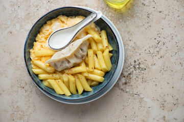 Bowl of korean tteokbokki or garaetteok with steamed dumpling and egg, horizontal shot on a beige granite background, above view