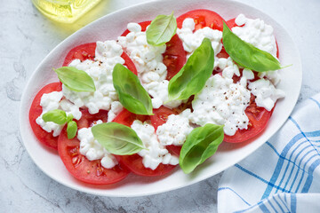 Caprese with cottage cheese, sliced fresh tomatoes and green basil, horizontal shot on a white stone background