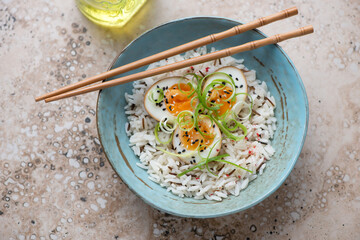 Marinated eggs with mixed rice and spring onion in a turquoise bowl, horizontal shot on a beige granite background, high angle view