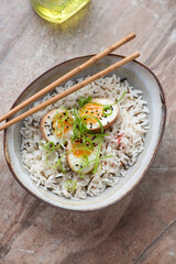 Bowl of mixed rice and soy-marinated eggs on a brown granite background, vertical shot, elevated view