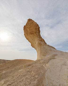 View of a solitary rock formation, sculpted by time and wind, standing stark against the pale sky and sandy ground, Zekreet, Al Sheehaniya Municipality, Qatar.