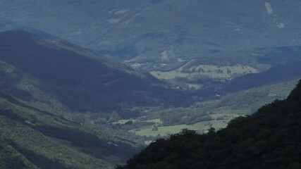 Cinematic 4K drone reveal of deep canyon valley using 7x telephoto lens. High bitrate broadcast quality master with layered mountain shadows and sunny spots.