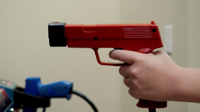Close-up of a hand gripping and using a red arcade light gun mounted on a shooter game cabinet, showing aiming and trigger interaction during classic indoor arcade gameplay, then placing gun back down