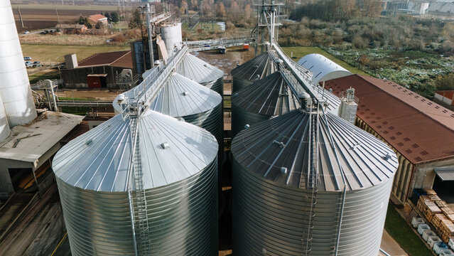 Aerial view of gleaming metallic silos standing tall against the backdrop of rustic buildings and verdant trees, blending industry with nature harmoniously, Sremska Mitrovica, Vojvodina, Serbia.