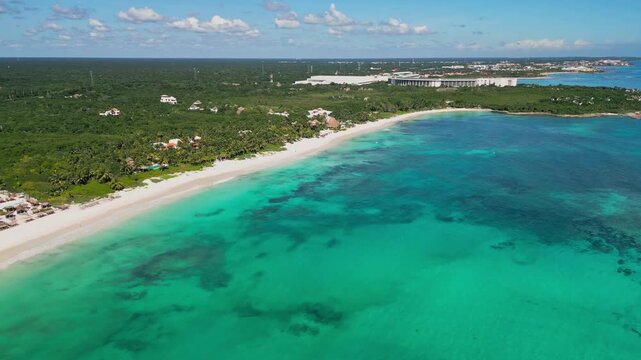 Drone footage of the turquoise Caribbean Sea and white sand beach at Xpu-Ha near Tulum, Quintana Roo, Mexico. Clear shallow waters meet lush tropical coastline under calm summer skies