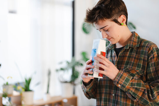 A young person in a plaid shirt holds a white bag, smelling the aroma of its contents with a focused expression. They are enjoying the fresh scent indoors.