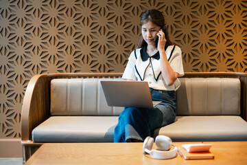 Professional woman multitasking with laptop and phone in a contemporary office setting, featuring a unique geometric wall pattern.