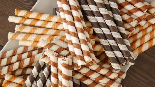 Pile of crispy striped wafer rolls with chocolate and vanilla cream filling slowly rotating.