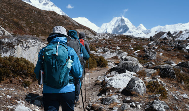Group of backpackers trekking Everest Base Camp along mountain trail among many large stones, snow-capped of mountains in the Nepal Himalayas.