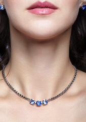Bijouterie on young female . Woman wears a chainlet with blue rhinestones and earrings.