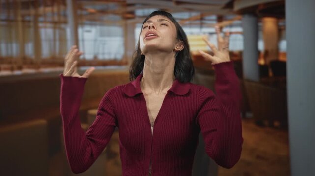 Hispanic woman in red sweater with crossed arms and raised gaze in a modern restaurant building; denial.