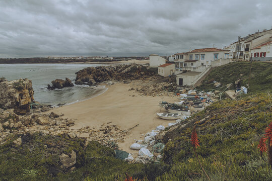 View of the sandy beach with boats and buildings under a cloudy sky on a coastline, Peniche, Leiria District, Portugal.