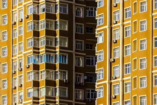 View of sunlit apartments in a towering building with rows of windows and air conditioning units casting shadows in the urban landscape, Aktau, Mangystau Region, Kazakhstan.