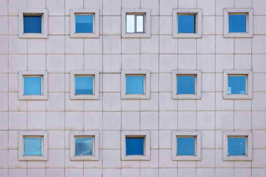 View of azure windows reflecting the sky, gridded across a neutral facade, a solitary window stands open, a stark contrast in Aktau, Mangystau Region, Kazakhstan.