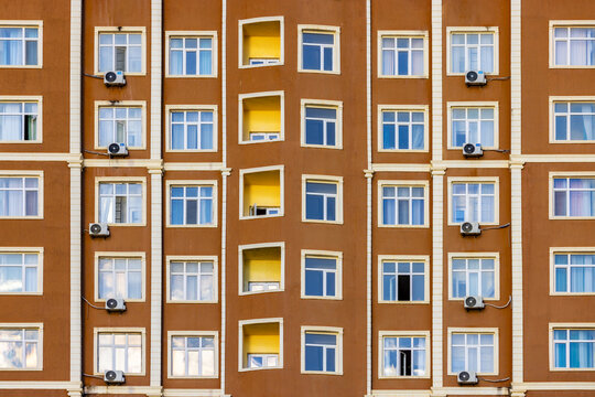 View of a symmetrical facade with brown walls, white window frames, and blue and yellow windows creating a geometric pattern, Aktau, Mangystau Region, Kazakhstan.