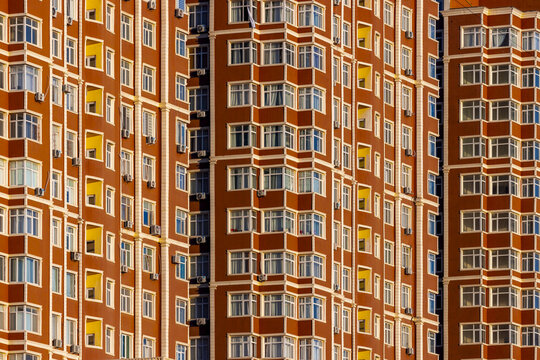View of the towering terracotta-colored building rises majestically, its symmetrical facade punctuated by rows of windows catching the light, Aktau, Mangystau Region, Kazakhstan.