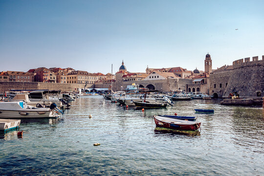 View of boats bobbing gently in the sun-kissed water, beneath the ancient stone walls and terracotta rooftops, a timeless tableau of maritime life, Dubrovnik, Dubrovnik-Neretva County, Croatia.