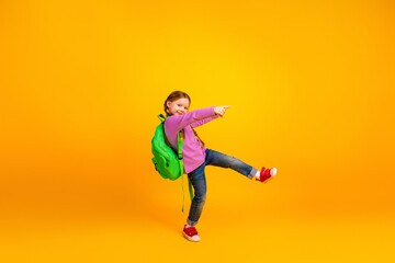 Obraz premium Young girl with green backpack jumping against yellow background smiling and pointing