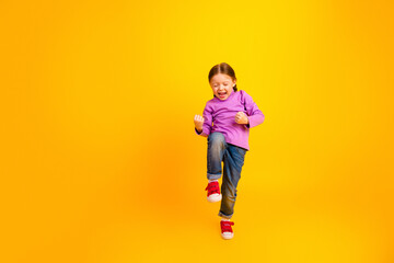 Obraz premium Joyful young girl jumps in purple shirt against bright yellow background