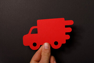 A close-up of a hand holding a red truck cutout against a black backdrop, conveying delivery and transportatio